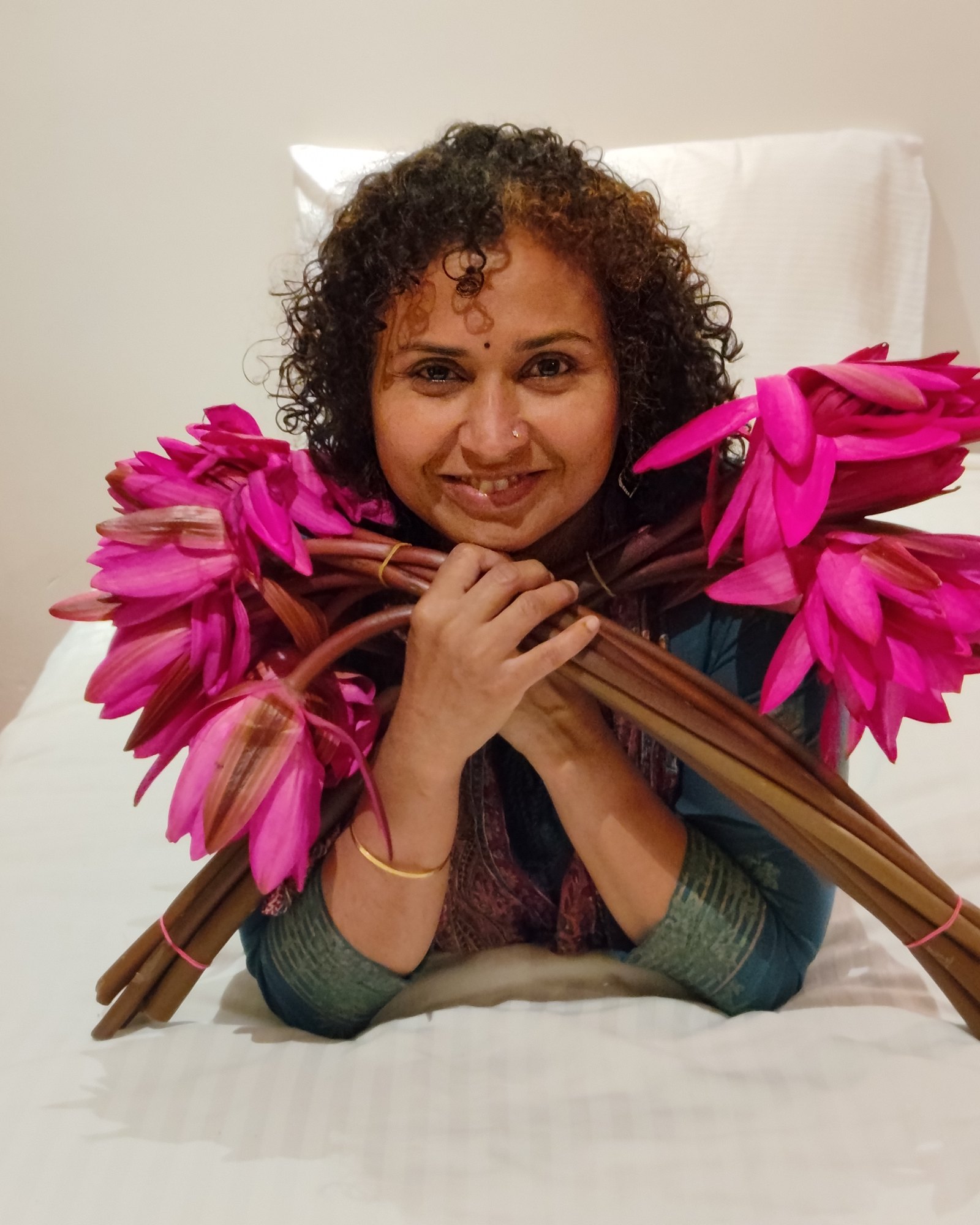 Chandni Krishnan smiling, resting her chin on her hands and holding two bunches of pink lotus flowers