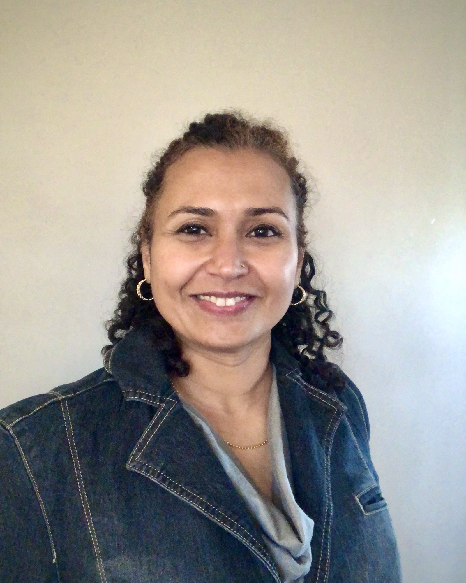 Chandni Krishnan smiling in a denim jacket against a pale wall
